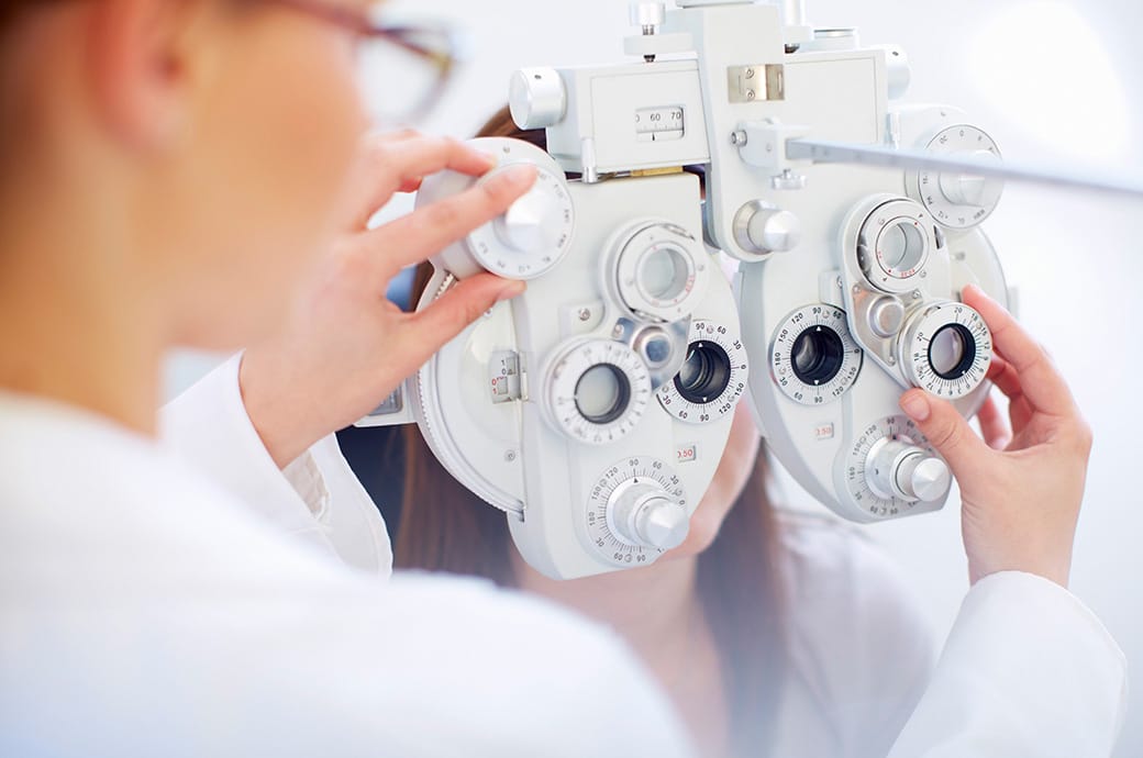 Fiatal nő foropter mögött, miközben a szemészeti szakember ellenőrzi látását egy látásvizsgálat során.